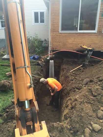 Worker in trench installing deck support while excavator digs